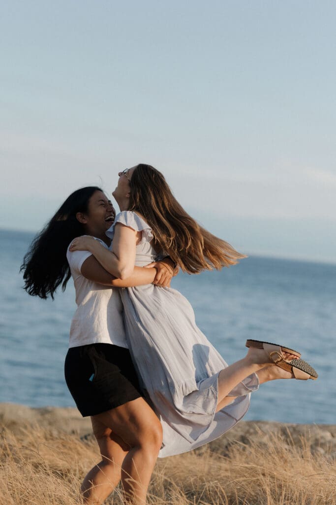 Newly engaged couple celebrating after a surprise proposal at Saxe Point Park with golden hour light and ocean views in Victoria BC