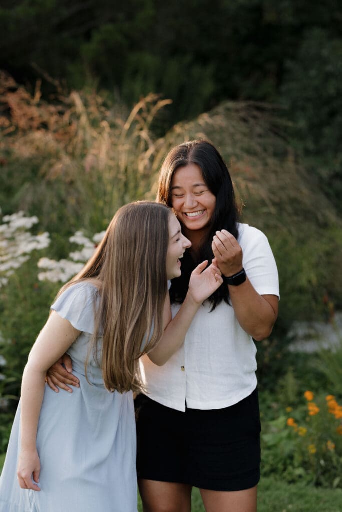 Engaged couple laughing in wildflowers and dry summer grass at Saxe Point Park during a golden hour proposal photography session in Victoria BC