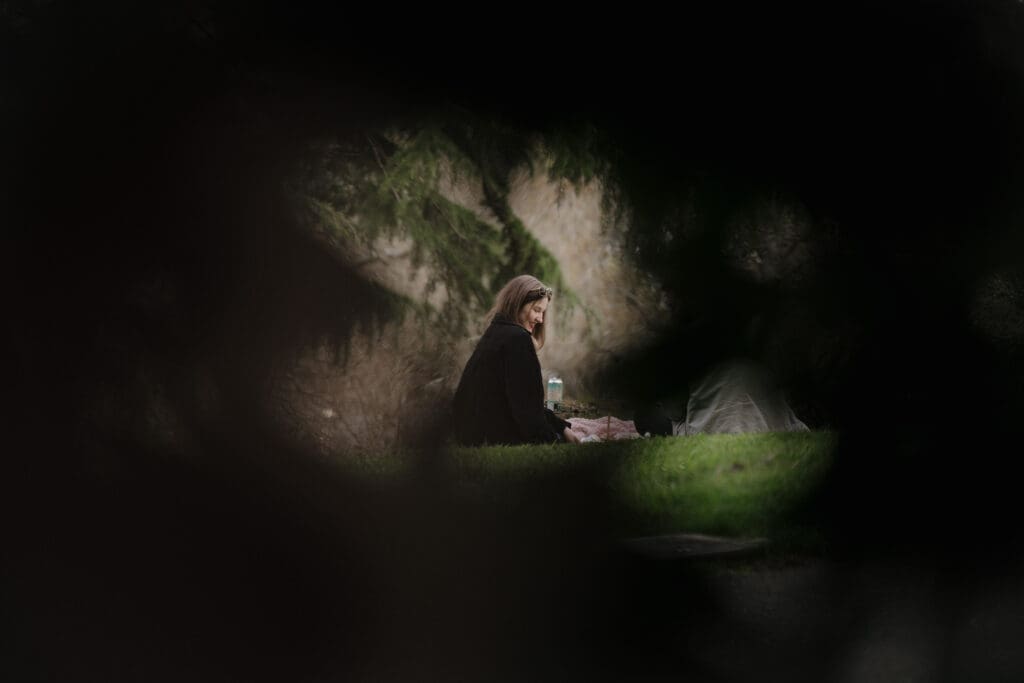 This cinematic image through the bushes of a woman sitting at a picnic in the gardens at Government House in Victoria BC was captured just before her surprise proposal by Victoria BC proposal photographer.