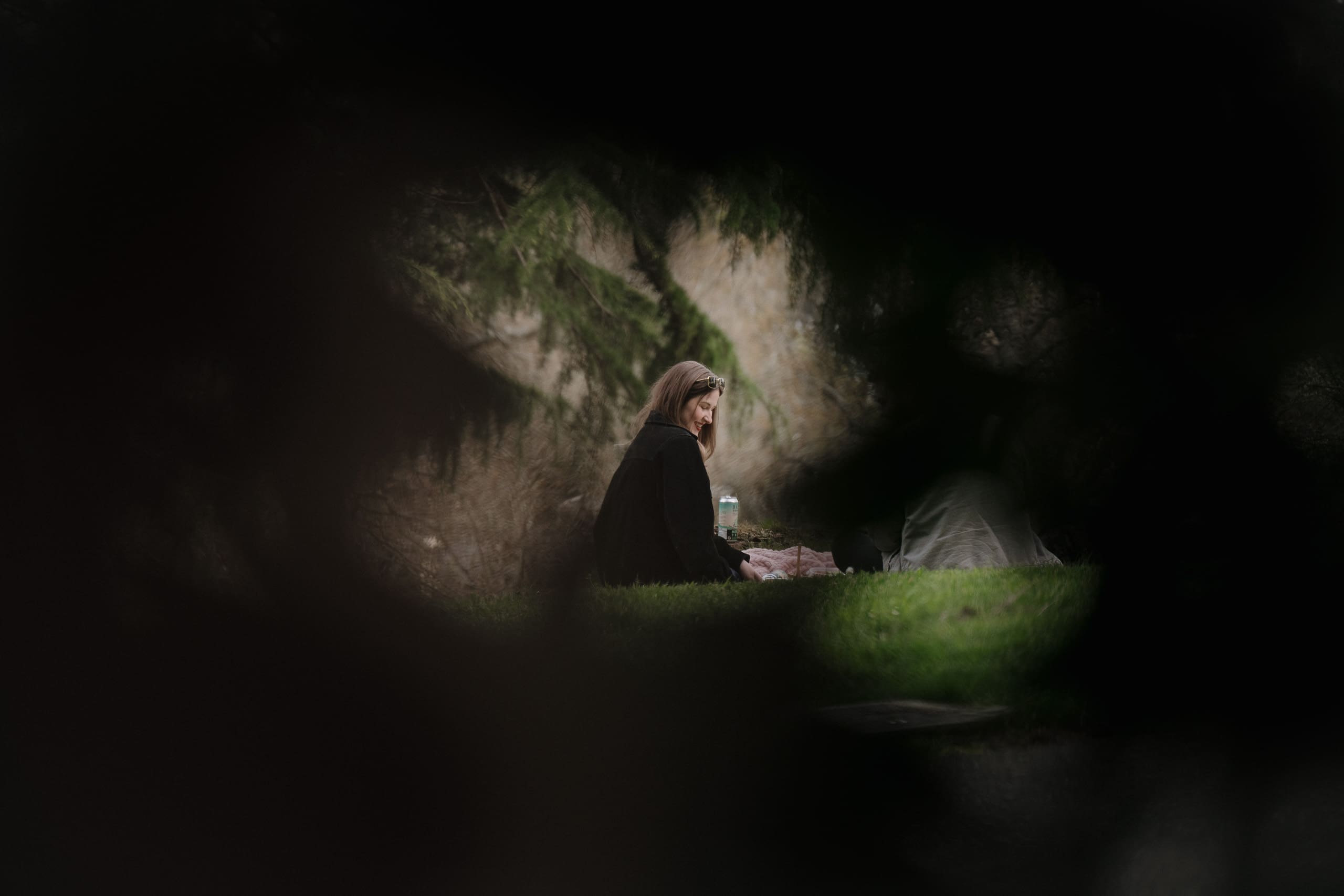 This cinematic image through the bushes of a woman sitting at a picnic in the gardens at Government House in Victoria BC was captured just before her surprise proposal by Victoria BC proposal photographer.