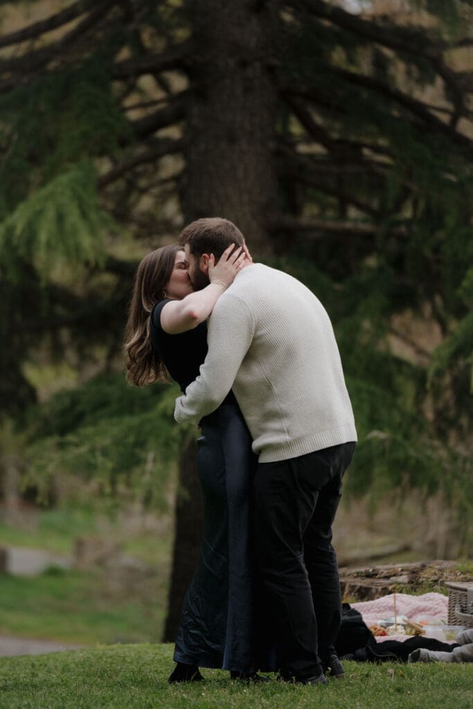 Newly engaged couple kissing together in the gardens of Government House in Victoria BC, candid proposal photography
