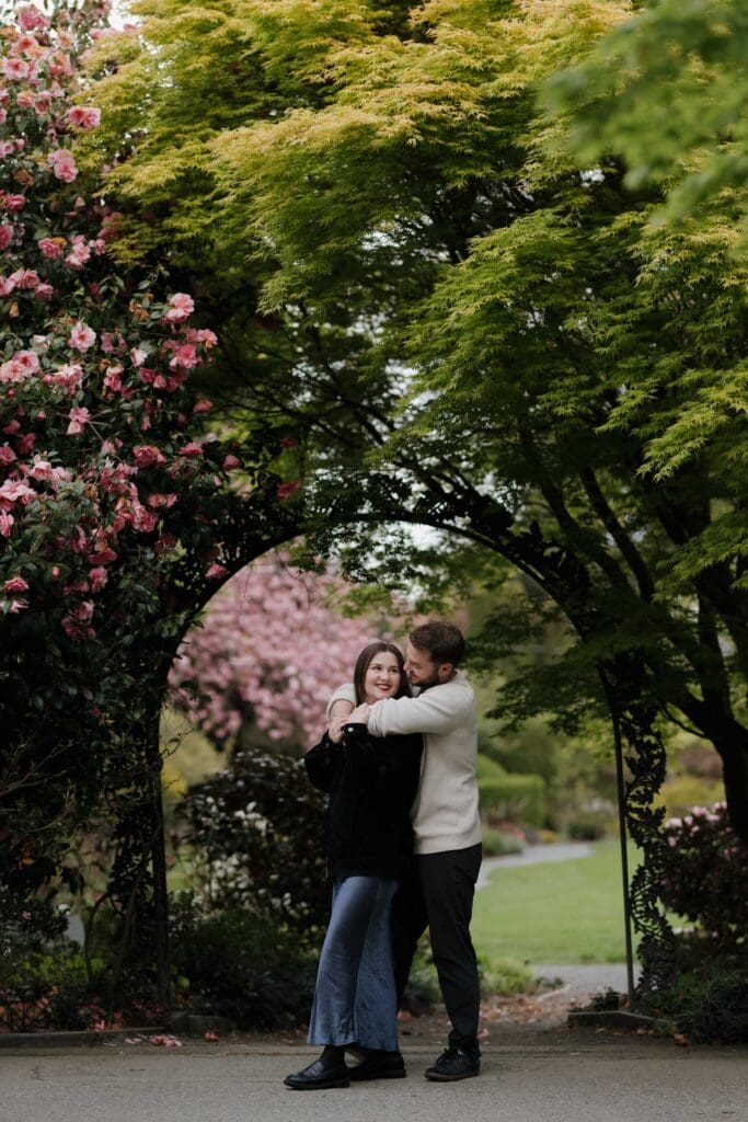 Couple embracing in Government House gardens Victoria BC after a surprise proposal, surrounded by spring blooms