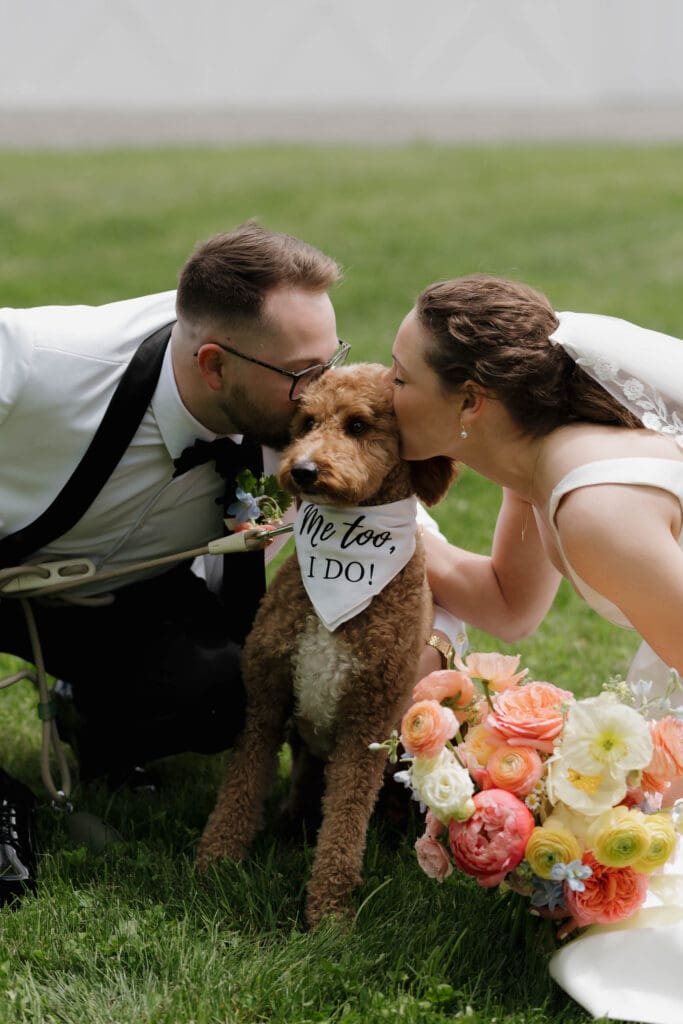 A bride and groom share a kiss with their golden doodle dog Lenny during their first look before their wedding.