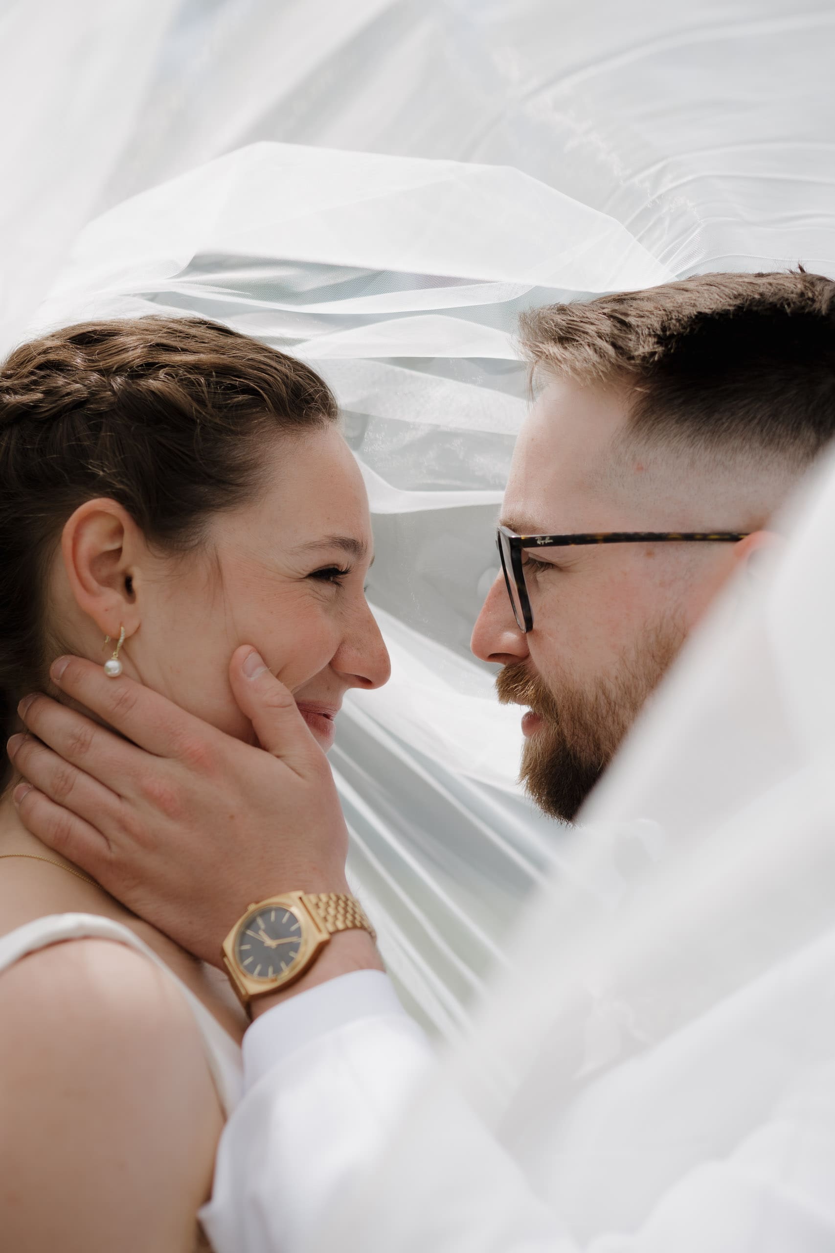 A groom holds his bride's face lovingly underneath the veil as they both smile to each other in excitement of becoming husband and wife.