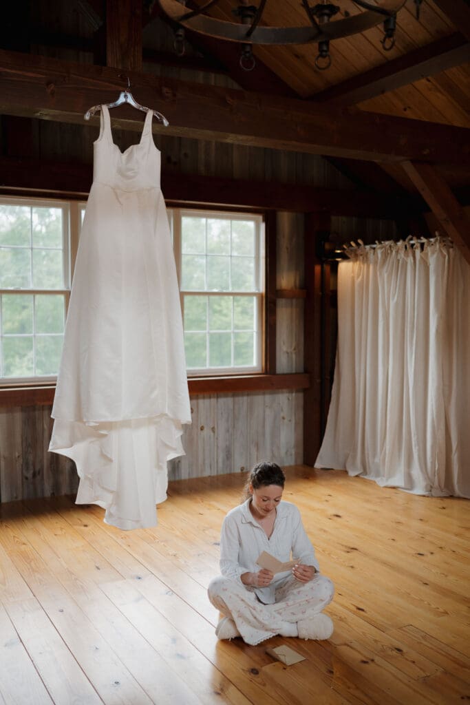 A bride is captured the morning of her wedding as she reads a letter from her soon to be husband. Her wedding dress is hanging beside her as she sits cross legged on the floor in her bridal pyjamas.