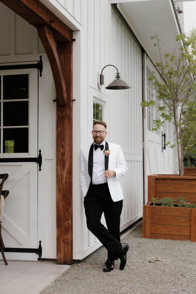 A groom waits outside a white building at Wildflower on Watts before his wedding in Honesdale PA. Captured by Hayley Zumkeller, travel wedding photography and videography team from Victoria BC Canada