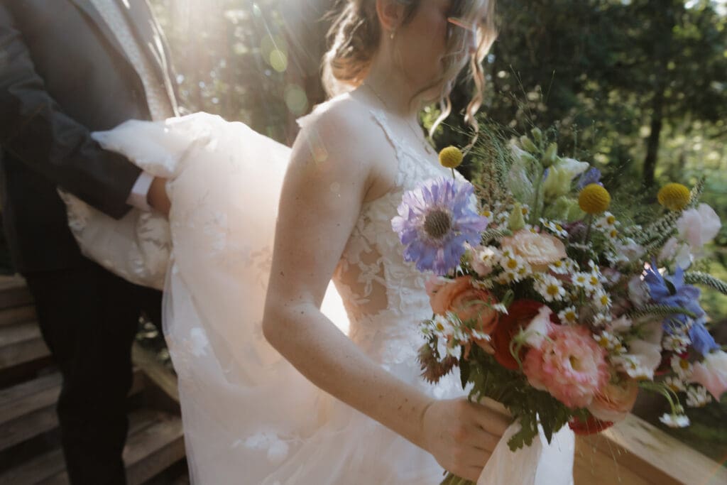 The later afternoon rays filter through the trees as this bride is walking down outdoor stairs to a private waterfall session with her groom after the ceremony.