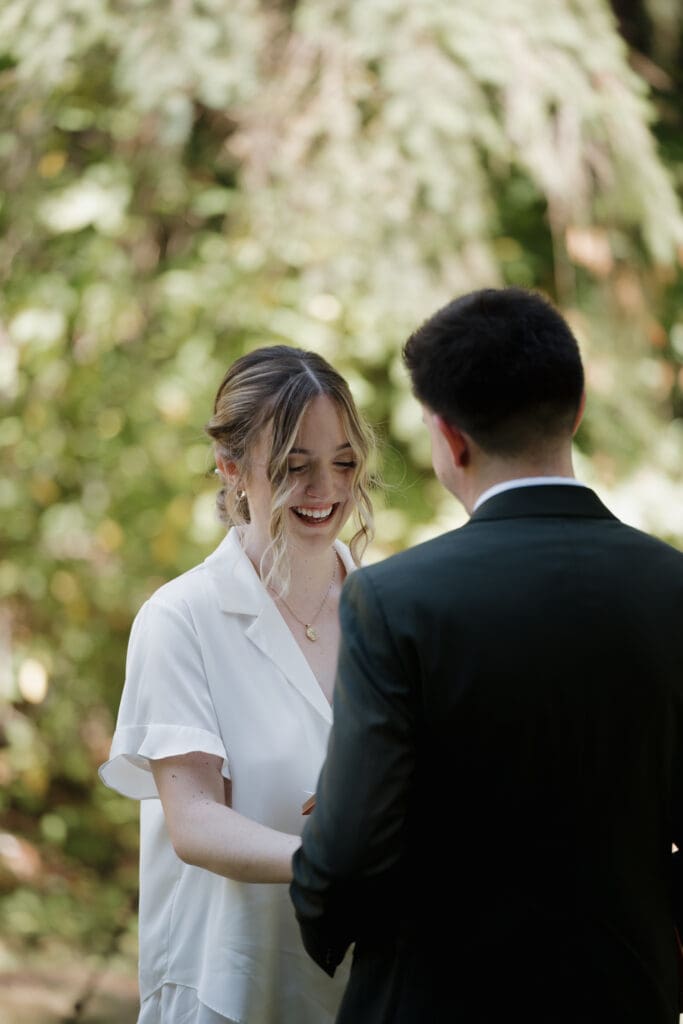 A bride smiles at her groom during their first look as they exchange private vows in Nanaimo BC. The bride wears white bridal pyjamas while the groom wears his wedding attire.