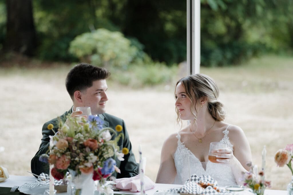 A bride and groom share a loving look during speeches at their wedding dinner outdoors on a private family property in Nanaimo BC. Captured by Hayley Zumkeller's Vancouver Island Wedding Videography team.
