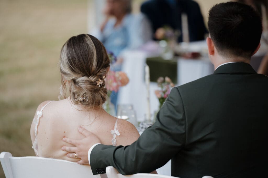 A new husband gently touches the back of his bride while they listen to speeches during their reception celebration before dinner in Nanaimo BC.