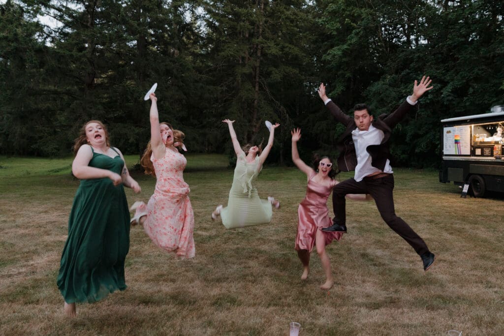 The bridal party jumps in the air during the outdoor reception of this private wedding on a family property in Nanaimo BC.