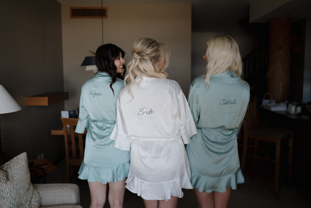 A bride and her bridesmaids have their back to the camera to show their custom made bridal robes that they wore while getting ready for the beach wedding in Tofino BC.