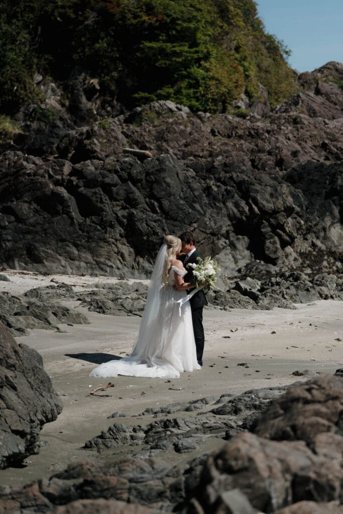 Tofino wedding photographer captures a bride and groom sharing a private moment following their beach wedding, surrounded by the rock and sand at Chesterman Beach.