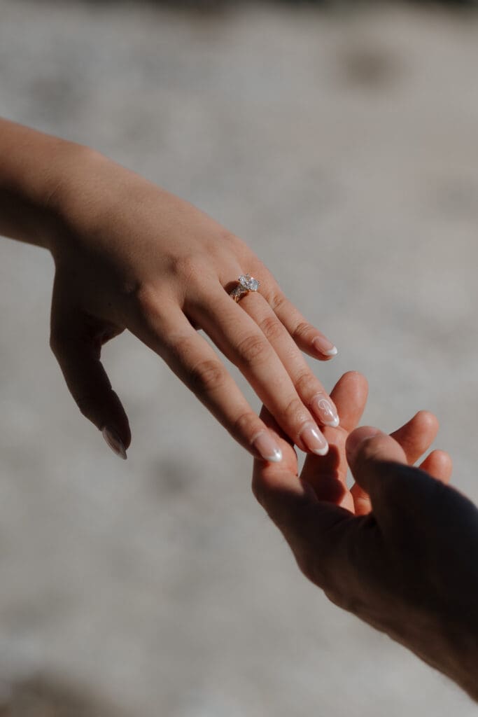 A newly married bride and groom touch hands on Chesterman beach, reaching for each other.