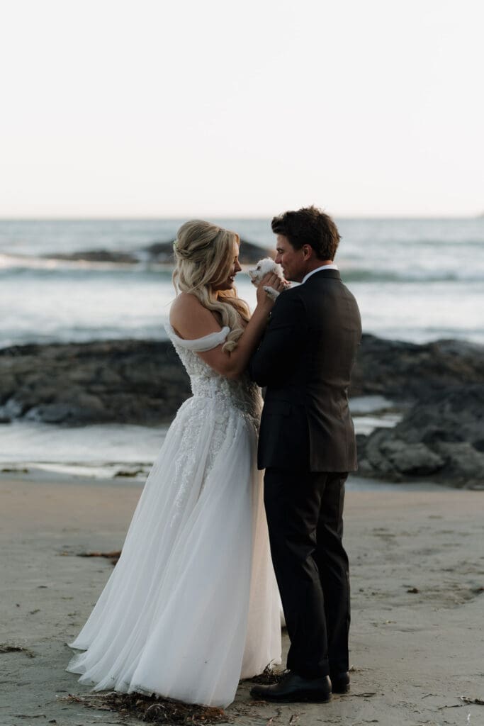 Tofino wedding photographer captures a bride and groom embracing their dog at the beach during golden hour