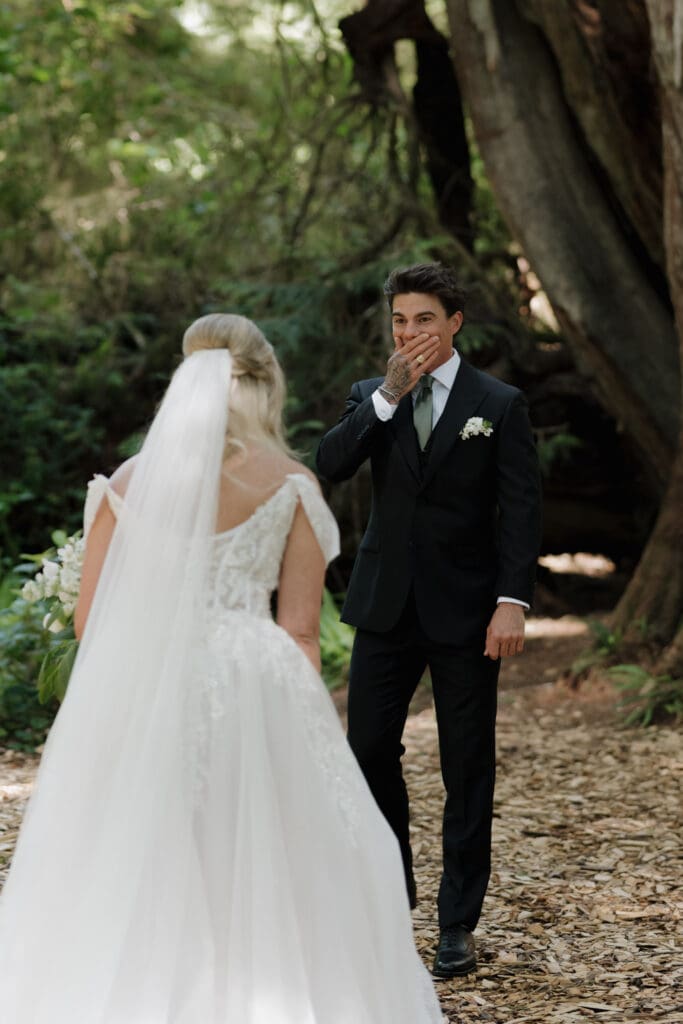 Bride and groom sharing their first look in the coastal rainforest near the Wickaninnish Inn in Tofino. Groom has his hand to his mouth in awe at seeing his bride.