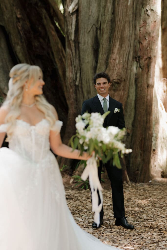 A bride looks behind her to her awaiting groom for their first look in the rainforest of Tofino BC.