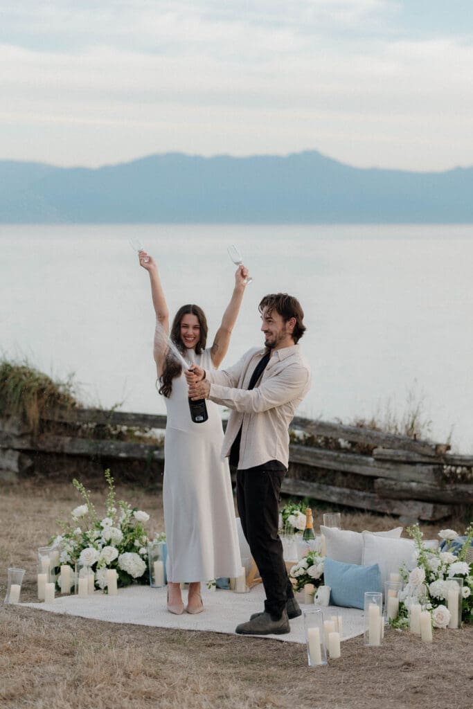 Styled picnic proposal setup with florals and candles, Victoria BC. Couple pops champagne to celebrate surprise proposal
