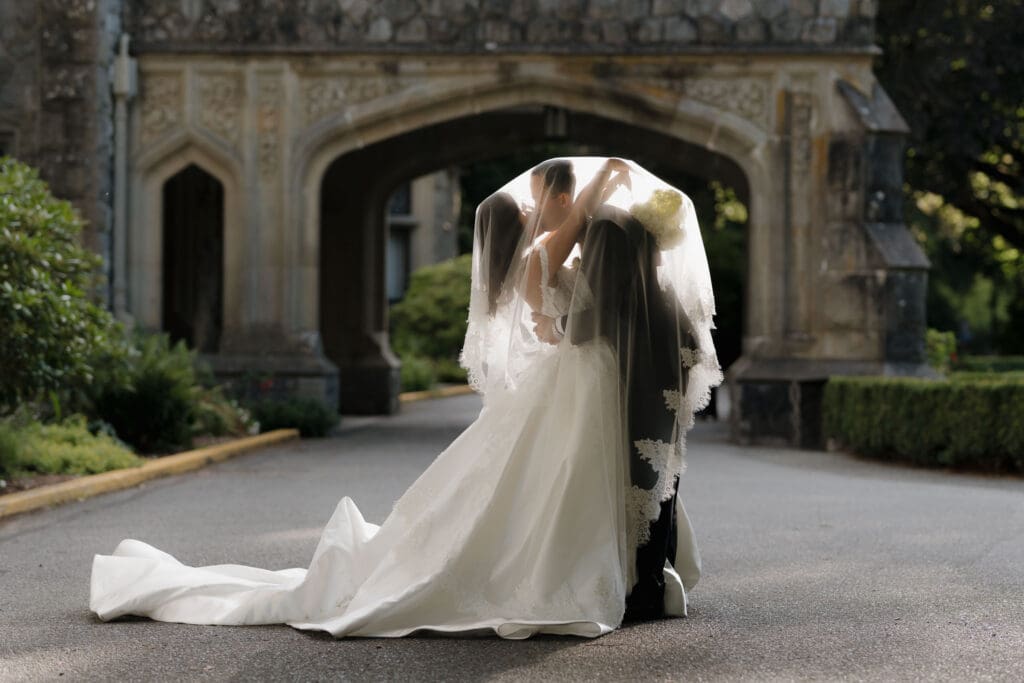 A bride and groom kiss outside Hatley Castle in this creative, under the veil shot.