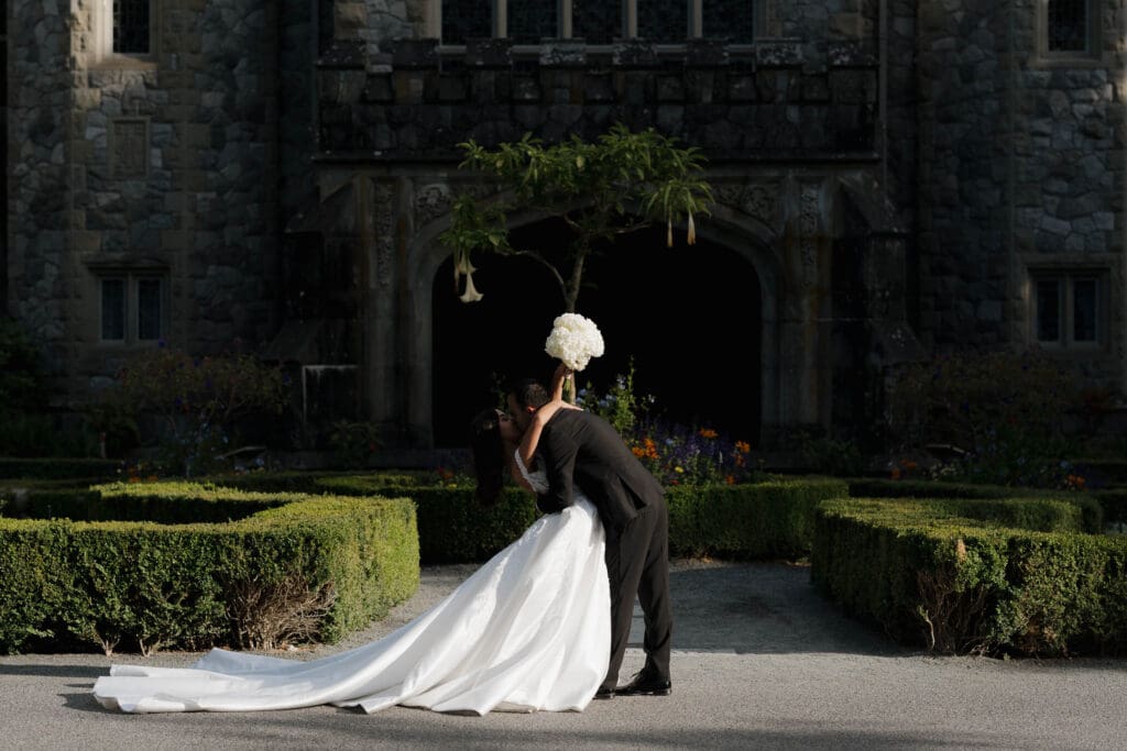 A groom dips his bride for a kiss outside their Victoria BC wedding venue Hatley Castle.