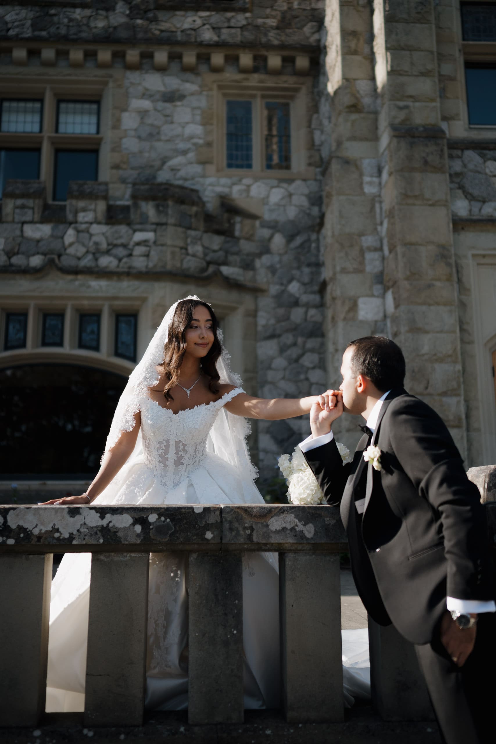 A groom kisses the hand of his bride with the majestic Hatley Castle in Victoria BC in the background.